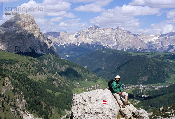 Wanderer ruht auf Alta Via Dolomiti (Via Ferrata) Wanderweg mit Corvara Dorf unten  Dolomiten  Südtirol  Italien  Europa