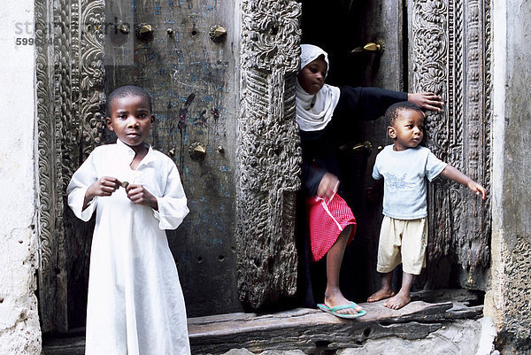 Junge muslimische Kinder vor eine kunstvoll geschnitzte Tür  Stone Town  Sansibar  Tansania  Afrika