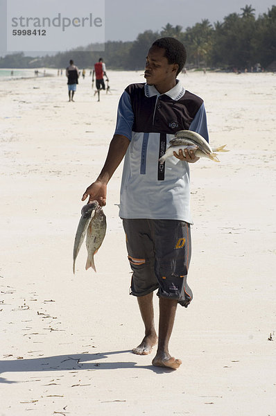 Ein Mann zu Fuß entlang des Strandes mit seinem Fang des Tages  Jambiani  Tansania  Ostafrika  Afrika