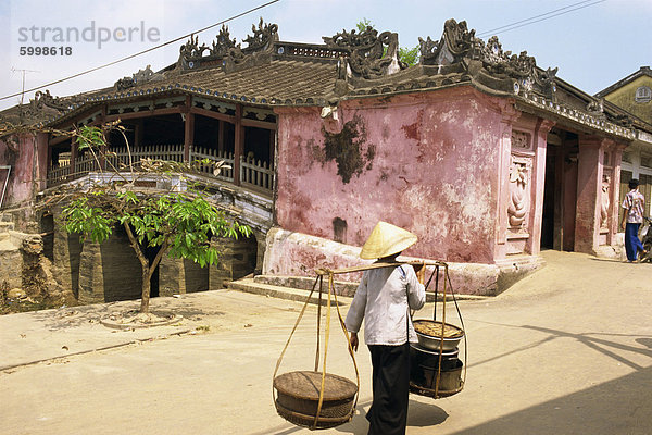 Frau  die Körbe auf einer Stange durch eine überdachte Brücke in Hoi An in Vietnam  Indochina  Südostasien  Asien