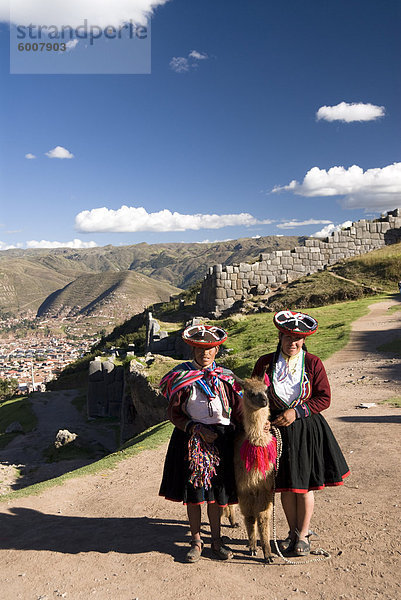 Inca Frauen in traditioneller Kleidung und Lamas  mit der Festung von Sacsayhuaman im Hintergrund  in der Nähe von Cuzco  Peru  Südamerika