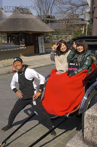 Rikscha Fahrer und zwei junge japanische Frauen in Rikscha mit roter Decke winken in die Kamera  Maruyama-Park  Higashiyama-Viertel  Kyoto  Kansai  Honshu  Japan  Asien