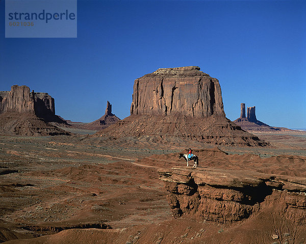 Eine Frau auf dem Pferderücken in der Wüste mit Felsformationen verursacht durch Erosion in den Hintergrund  im Monument Valley  Arizona  Vereinigte Staaten von Amerika  Nordamerika