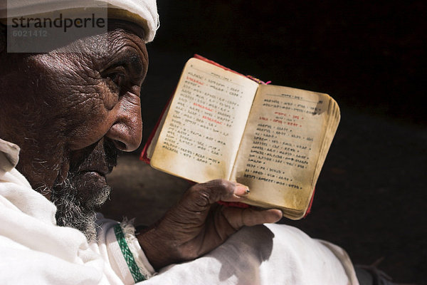 Alte Mann tragen traditionelle Gabi (weißes Tuch) sitzen in der Sonne lesen Heilige Bibel  an Kirche von Bet Medhane Alem (Retter der Welt)  Weltkulturerbe  Lalibela  Äthiopien  Afrika