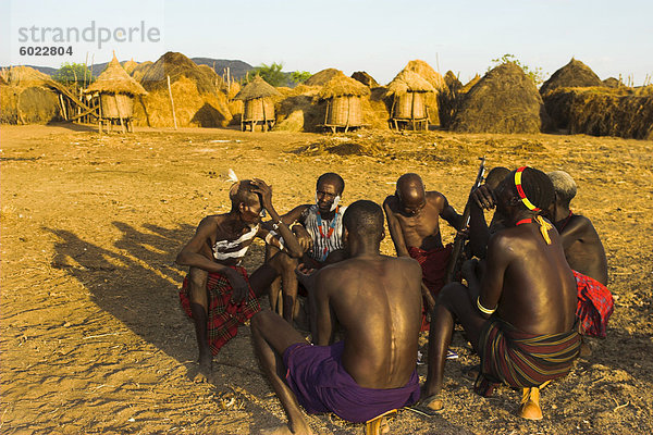 Karo ältesten sitzen mit Gewehren auf hölzernen Kopf-Resten mit Kalaschnikow  Kolcho Dorf  unteren Omo-Tal  Äthiopien  Afrika