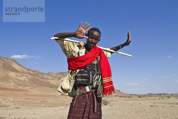 Ein junger einheimischer Mann Grinnig frech und hält einen Stock  Lac Abbe  Dschibuti  Afrika