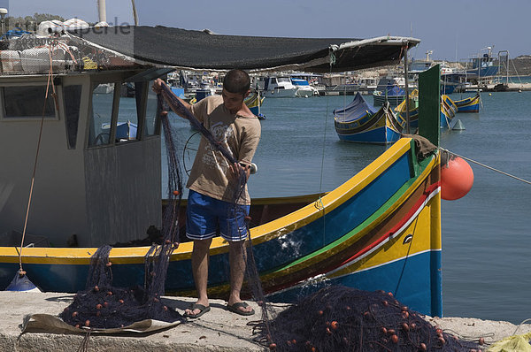 Aussortieren Netzes mit hell gefärbt Fischerboote namens Luzzus an Marsaxlokk  ein Fischerdorf  Malta  Mittelmeer  Europa