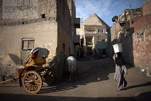 Eine Mädchen trägt einen Eimer mit Wasser durch die Gassen der Vorstadt von Gizeh  im Schatten der Pyramiden  Kairo  Ägypten  Nordafrika  Afrika