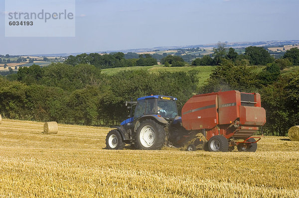 Traktor sammeln Heuballen zur Erntezeit  gesehen von den Cotswolds Weg Fußweg  The Coltswolds  Gloucestershire  England  Vereinigtes Königreich  Europa