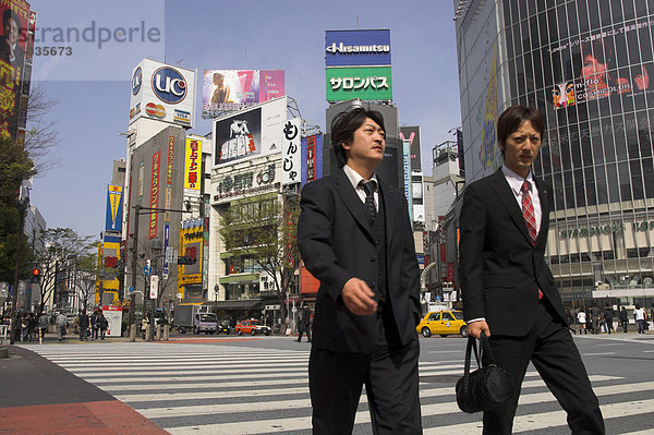 Gut gekleidet zwei junge Männer gehen auf Zebrastreifen mit Werbeplakaten und riesigen video-Bildschirm im Hintergrund  Shibuya  Tokyo  Honshu  Japan  Asien