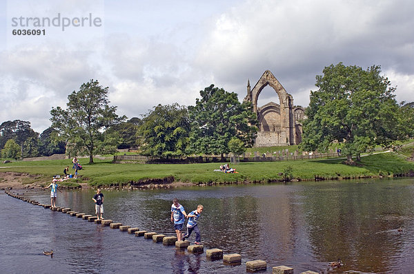 Kinder überqueren das stepping Steine über den Fluß Wharfe bei Bolton Abbey  Wharfedale  Yorkshire Dales National Park  Yorkshire  England  Großbritannien  Europa