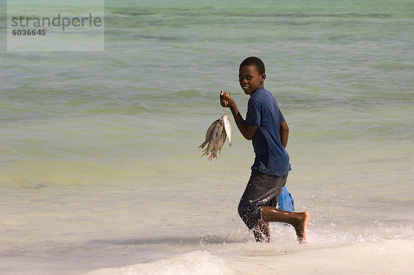Ein Junge unter im Meer mit seinem kürzlich gefangenen Fisch in der Hand  Jambiani  Tansania  Ostafrika  Afrika