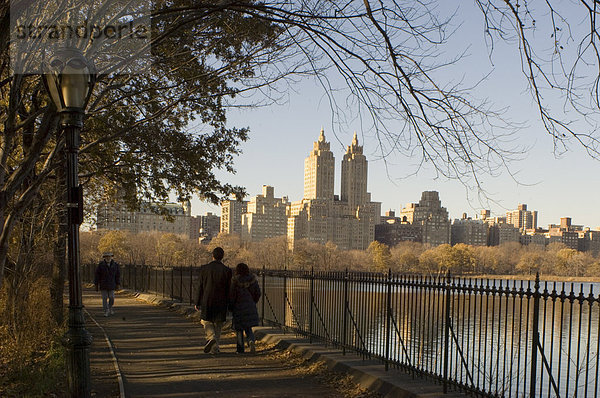 Menschen Wandern neben der Echsenkessel im Central Park im Winter mit hohen Gebäuden von Central Park West in den Hintergrund  New York City  Vereinigte Staaten von Amerika  Nord Amerika