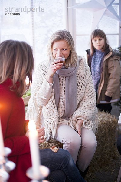 Frau trinkt mit zwei Mädchen in Winterkleidung im Gewächshaus