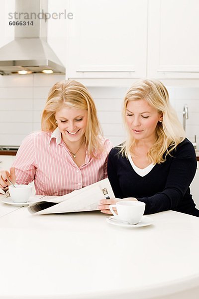 Zwei junge Frauen lesen Zeitung in Küche