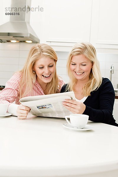 Zwei junge Frauen lesen Zeitung in Küche