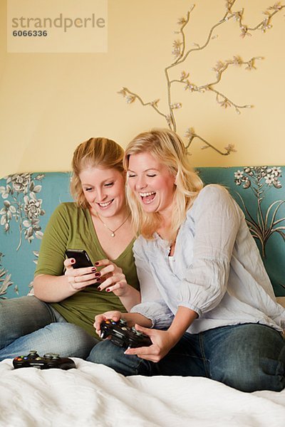 Zwei junge Frauen mit Handy im Schlafzimmer