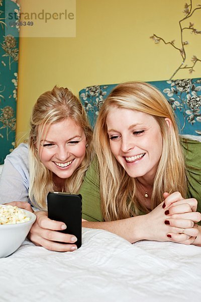 Zwei junge Frauen mit Handy im Schlafzimmer