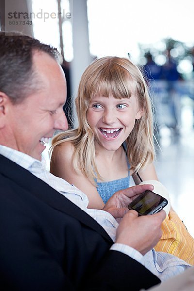 Vater mit Tochter sitzen am Flughafen und am Handy spielen