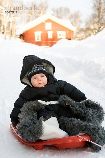 Baby-Mädchen  die im Winter auf Schlitten gleiten