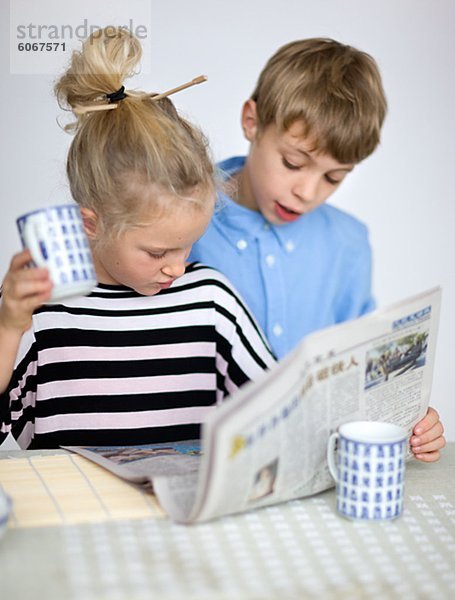 Porträt der jungen und Mädchen lesen Zeitung am Tisch