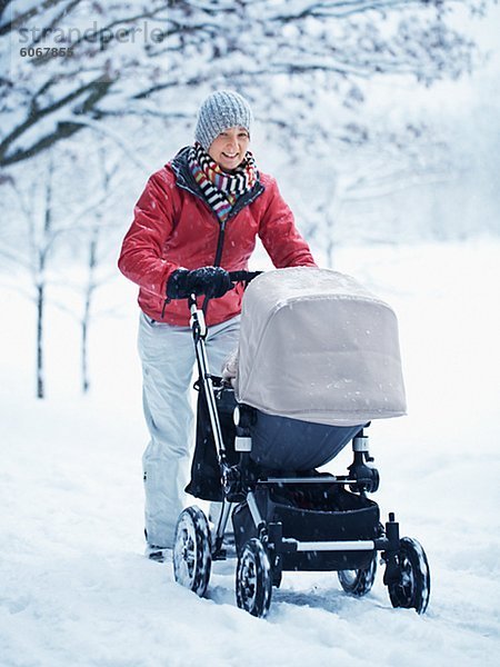 Lächelnde Mutter Wandern mit Kinderwagen in Winterlandschaft