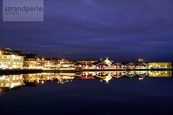 Beleuchtete Gebäude am Hafen im Wasser reflektiert