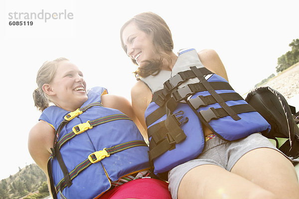 sitzend  Tag  Lifestyle  lächeln  grün  Jacke  Fluss  blau  Kajak  2  Mädchen  Yellowstone Nationalpark  lachen