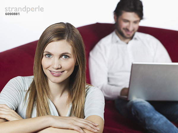 Frau lächelt  Mann benutzt Laptop im Hintergrund