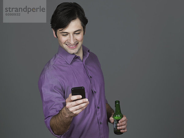 Junger Mann mit Bierflasche und Handy  lächelnd