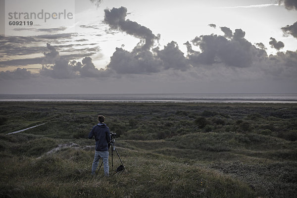 Niederlande  Mann steht mit Kamera an der Nordsee