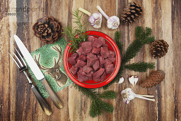 Rohes Hirschfleisch in Würfeln auf Keramikteller mit Zutaten und Weihnachtsdekoration