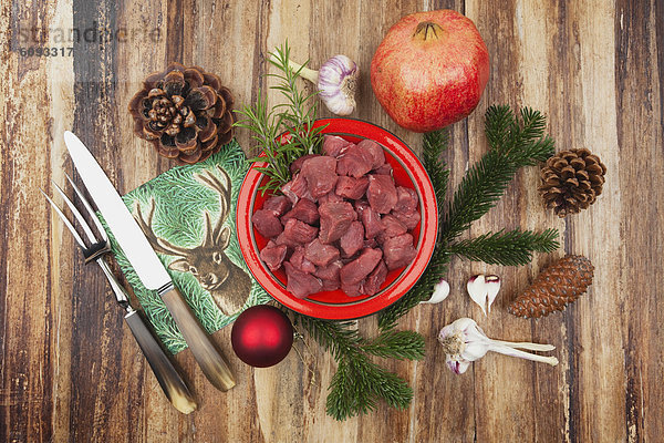 Rohes Hirschfleisch in Würfeln auf Keramikplatte mit Granatapfel und Weihnachtsdekoration