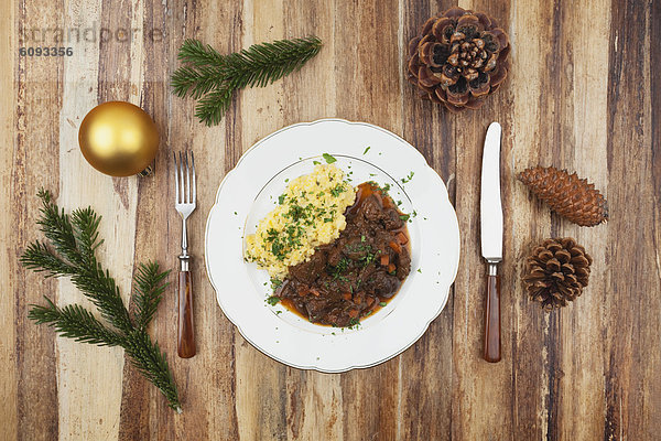 Teller mit gekochtem Hirschgulasch mit Kartoffelpüree und Weihnachtsdekoration auf Holzuntergrund