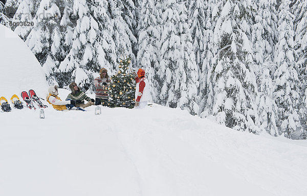 Österreich  Salzburg  Männer und Frauen im Winter am Weihnachtsbaum sitzend