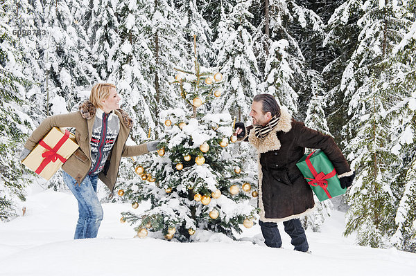 Österreich  Salzburger Land  Paar hält Weihnachtsgeschenk im Schnee  lächelnd