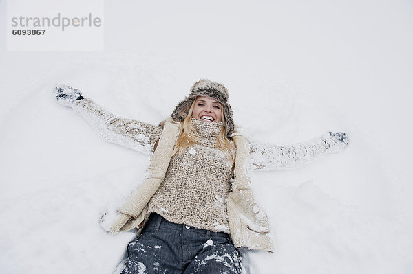 Österreich  Salzburger Land  Mittlere erwachsene Frau auf Schnee liegend  lächelnd