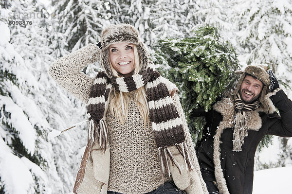Österreich  Salzburger Land  Mann und Frau gehen durch den Schnee  während der Mann einen Weihnachtsbaum trägt.
