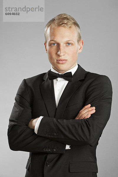 Junger Mann im schwarzen Anzug vor grauem Hintergrund