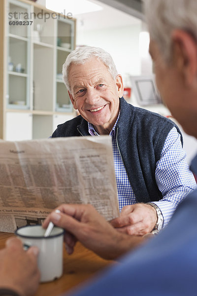 Älterer Mann  der Zeitung liest  ein anderer Mann  der Kaffee rührt.