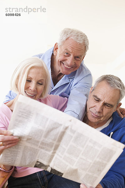 Ältere Männer und Frauen lesen Zeitung  lächelnd