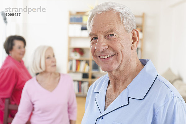 Älterer Mann lächelnd  Frauen im Hintergrund stehend