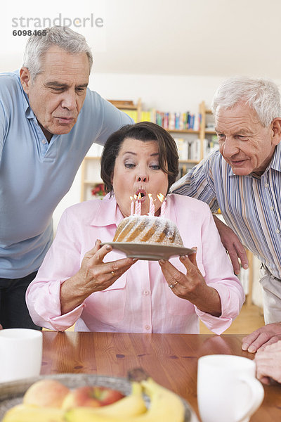 Ältere Männer und Frauen  die Kerzen auf Kuchen ausblasen.