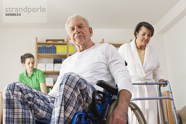 Älterer Mann auf Rollstuhl sitzend  Frau mit Gehgestell