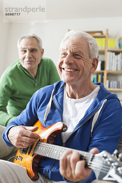 Senior Mann spielt E-Gitarre  Mann sitzt im Hintergrund