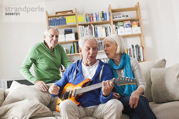 Senior man playing electric guitar  man and woman sitting besides