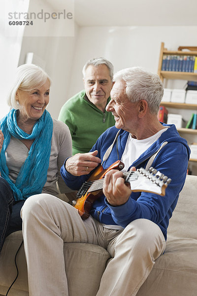Senior man playing electric guitar  man and woman sitting besides
