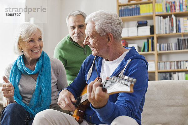 Senior Mann spielt E-Gitarre  Mann und Frau sitzen daneben