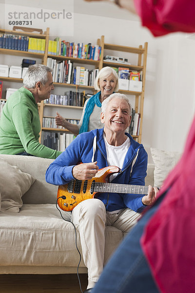 Senior man playing electric guitar  man and woman in background
