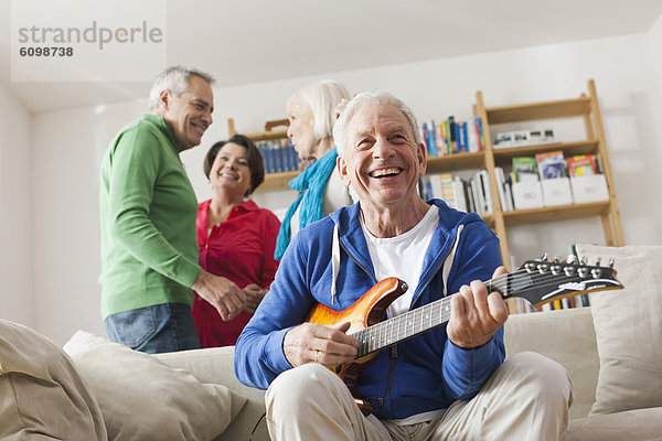 Senior Mann spielt E-Gitarre  Mann und Frau im Hintergrund